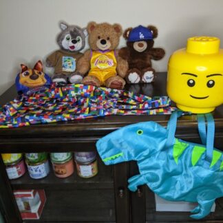 Lot # 113 - Kids Plush lot with Lego head container, bags, and paw patrol hat.